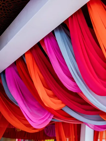 A beautiful ceiling of draped fabric in contrasting shades of red, pink, orange, and grey. This creates a soft, colorful canopy over the Mehendi celebration space.