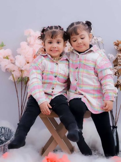 Two sisters sitting together on a stool in a cozy, rustic setup. We offer a variety of themes and backdrops for our studio sessions.