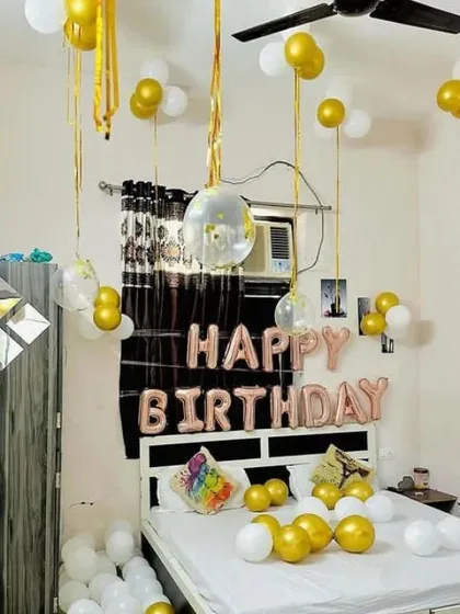 A simple and elegant birthday room decoration. This setup includes "Happy Birthday" foil letters in rose gold, with gold and white balloons on the bed and floor.
