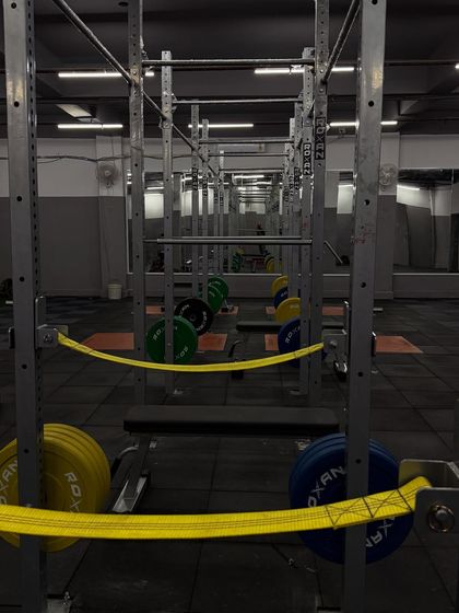 A perspective from within the power rack, the place where raw strength is forged. The gym is equipped with high-quality barbells and bumper plates to handle the heavy loads required for professional athlete training.