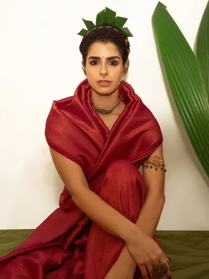 A modern interpretation of traditional aesthetics, blending a classic red silk sari with a contemporary leaf crown. The clean, white background puts full emphasis on the unique styling and the model's strong presence.