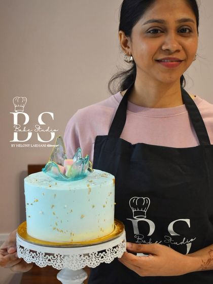 A student proudly displays her light blue cake with gold accents and a multi-colored isomalt piece, showcasing her new skills.
