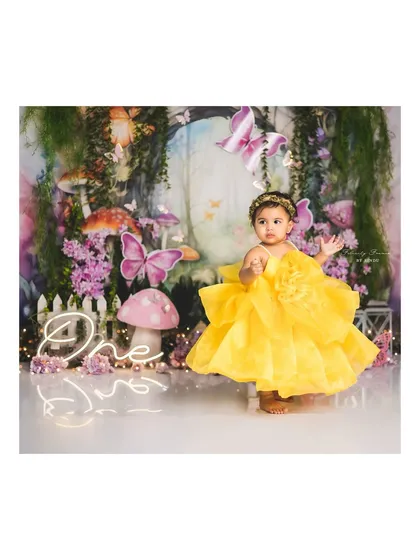 A little fairy in a yellow dress, standing in her magical forest. The "One" sign adds a special touch for a first birthday.