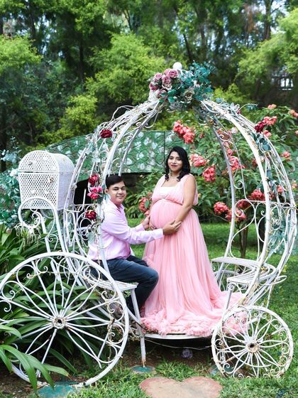A true fairytale moment. This couple is posing in a beautiful, ornate white carriage in a garden, perfect for a princess-themed maternity shoot.