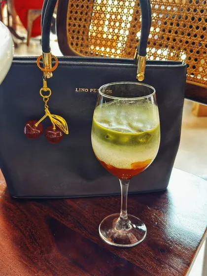 A detail shot focusing on my handbag with a cute cherry charm, placed next to a layered drink. This highlights accessories in a natural cafe setting.