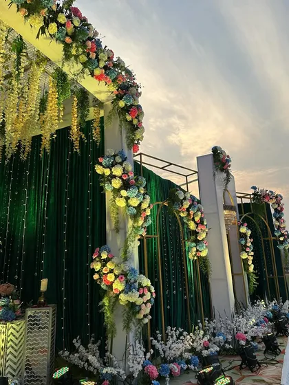 Another angle of the emerald and gold reception stage, highlighting the cascading floral arrangements and the dramatic evening sky.