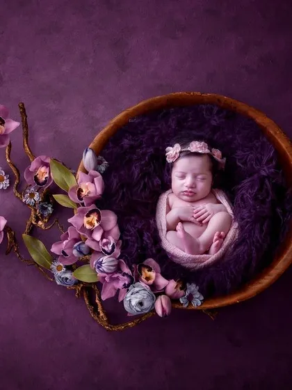 Inspired by nature, this portrait features a newborn nestled in a wooden bowl, adorned with a cascade of purple orchids. The rich color palette and organic elements come together to create a truly artistic and memorable image.