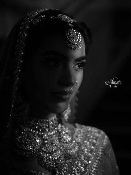 A dramatic black and white bridal portrait. The play of light and shadow highlights her intricate jewelry and creates a moody, timeless feel.