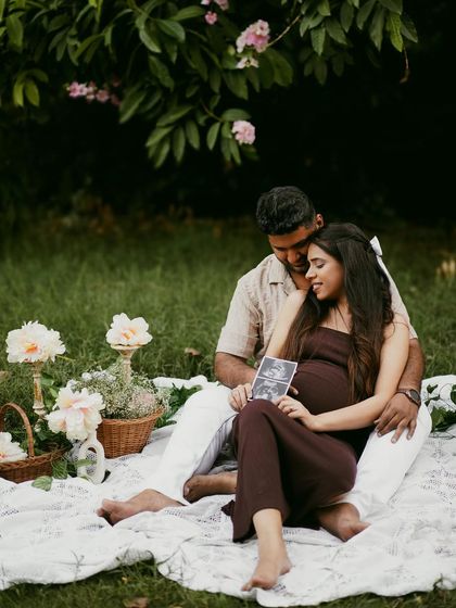 A romantic picnic setup in a garden, where the couple shares a quiet moment looking at their sonogram pictures.