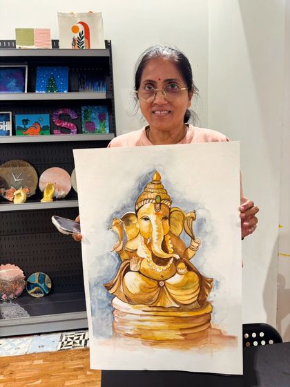 A participant holds her large, detailed watercolor painting of Lord Ganesha, demonstrating the beautiful shading and form achieved in our art class.