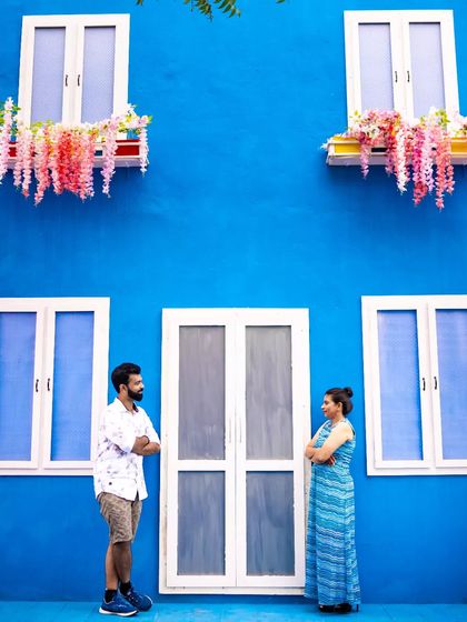A couple stands against a bright blue wall with charming windows, creating a vibrant and symmetrical composition. We have an eye for architectural details that make great photo backdrops.