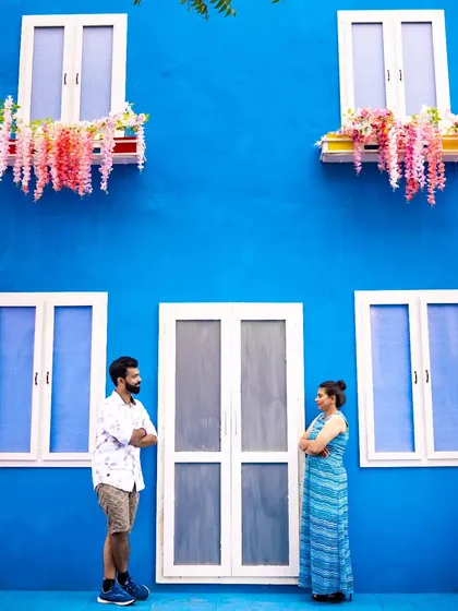 A couple stands against a bright blue wall with charming windows, creating a vibrant and symmetrical composition. We have an eye for architectural details that make great photo backdrops.
