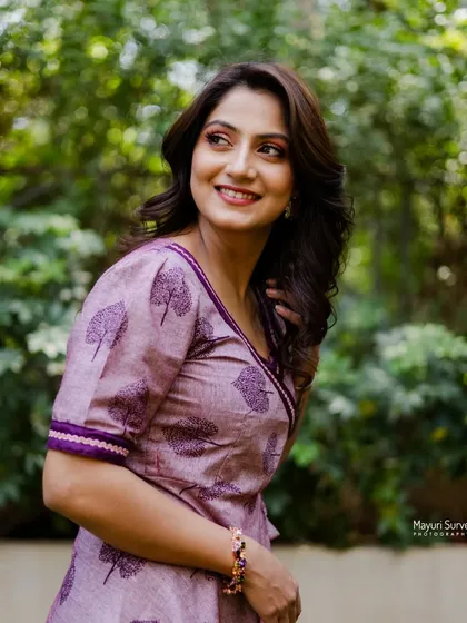 A joyful and candid shot. The actress looks away with a big smile, capturing a moment of genuine happiness in a natural, outdoor setting.
