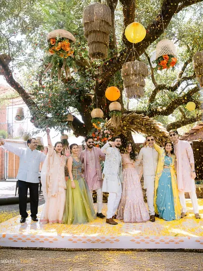 The couple with their friends and family, celebrating under a shower of flower petals at their outdoor Haldi ceremony.