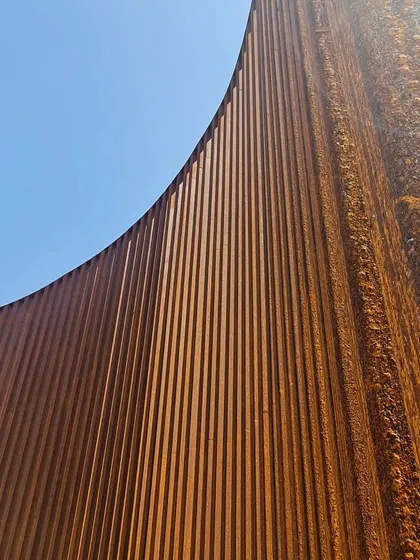 The rich, rusted texture of the Corten steel provides a warm, earthy contrast to the blue sky.