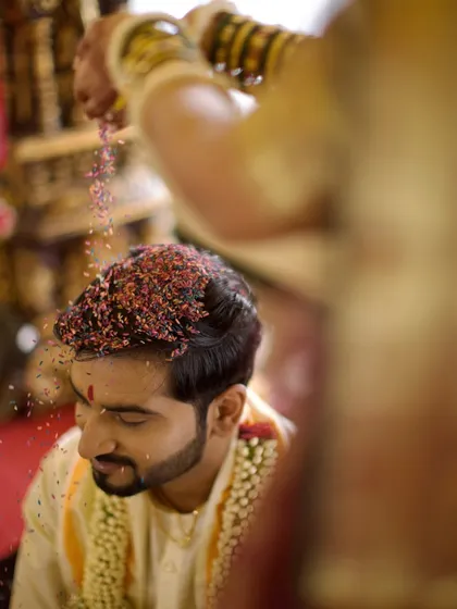 A close-up of the groom during the 'talambralu' ritual, capturing the texture of the colored rice and his serene expression.