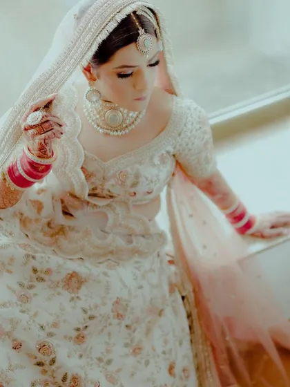 A top-down view of a bride in a stunning white floral lehenga, wearing a pearl and polki choker set. A unique and elegant choice for a day wedding.