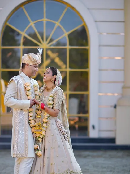A beautiful portrait of the couple in their day-wedding attire, sharing a loving gaze in front of a grand, sunlit building.