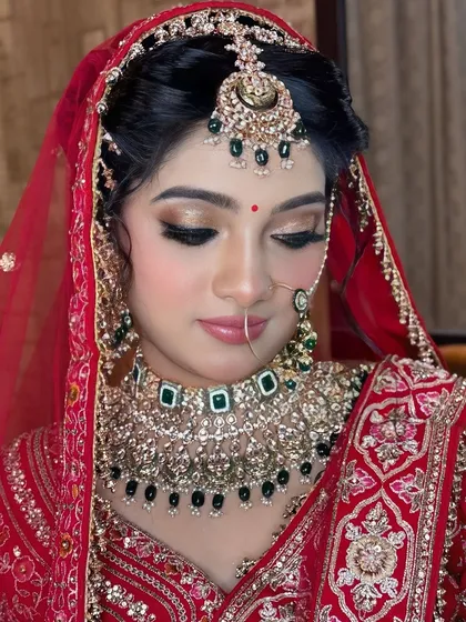 A close-up showcasing the detailed eye makeup with golden shimmer and a soft pink lip, perfectly complementing the bride's red and gold outfit.