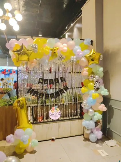 A pastel-colored balloon arch with a silver shimmer curtain, creating a fun photo backdrop for a first birthday.