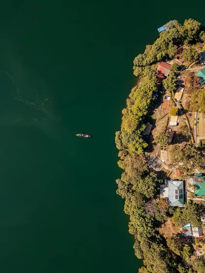A top-down view of the lake's edge, contrasting the deep green water with the lush shoreline dotted with houses.