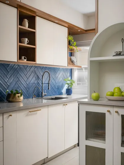 A detail of the 'Palaash' kitchen, showing the contrast between the bold blue backsplash, neutral cabinets, and an arched crockery unit with fluted glass.