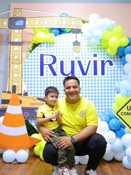 A father and son, matching in yellow shirts, pose proudly in front of their construction party setup.