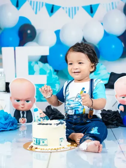 A fun and memorable "Boss Baby" themed cake smash for a first birthday. This shot captures the pure, messy joy of a baby enjoying his first taste of cake in a creative, fully-styled setup.