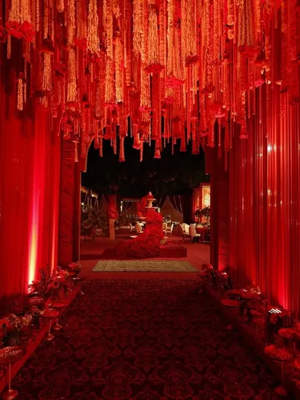 This dramatic crimson tunnel, with its ribbed walls and ceiling of hanging florals, was designed to create an immersive experience, leading guests toward the main event.