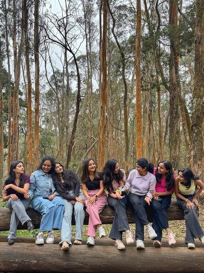 A group of girls sharing a laugh while sitting on a log in the Kodaikanal forest.