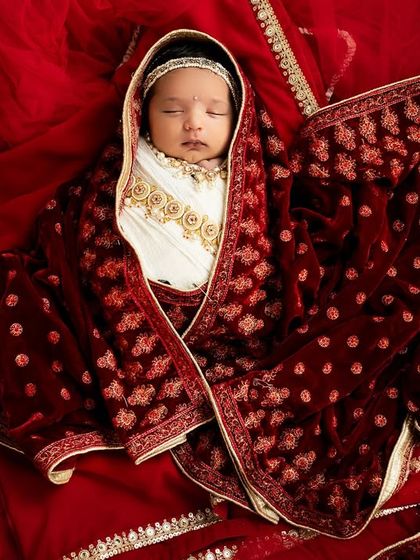 A duplicate of image 89, showing a precious newborn baby girl styled as Radha, wrapped in an ornate red velvet cloth.