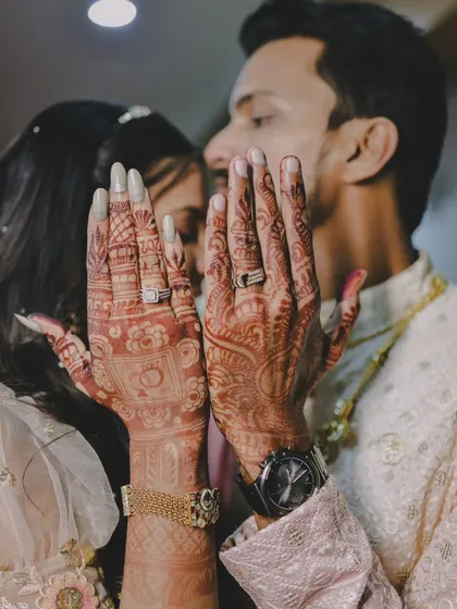 A duplicate of the creative shot showing the couple's henna-adorned hands and rings.