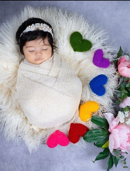 Another variation of the rainbow hearts theme, this overhead view shows the baby peacefully sleeping in a nest of soft fur. The arrangement of hearts and flowers adds a sweet, artistic touch.