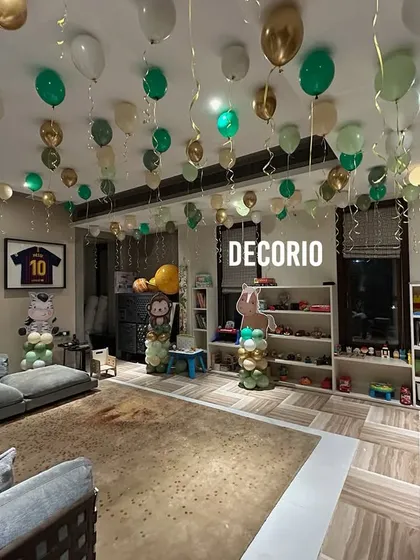 A full room decorated for a jungle-themed birthday party. Green, gold, and white balloons float from the ceiling, creating a canopy effect that transforms the entire space.