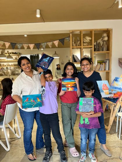 A family group holds up their finished paintings, each one a unique expression of their personality. We love seeing families bond over a shared love for creativity.
