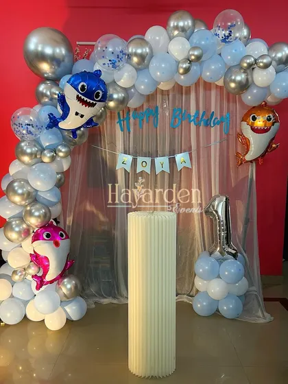 A cute Baby Shark theme for a first birthday. This home setup includes a balloon arch with character foil balloons and a sheer curtain backdrop.