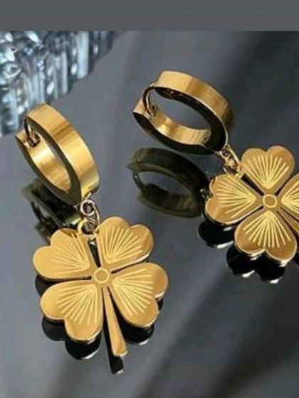 These dangle earrings feature a four-leaf clover charm with an etched sunburst pattern, hanging from a solid gold-tone hoop.