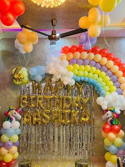 A classic Unicorn theme party at home, with a rainbow balloon arch over a silver fringe backdrop and unicorn balloon pillars.