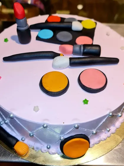 A glamorous and fun makeup-themed cake. Topped with edible fondant versions of lipstick, eyeshadow palettes, and brushes, this is the perfect cake for a beauty lover's birthday.