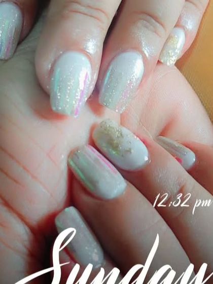 A white nail set with accents of gold foil and iridescent flakes for a textured, artistic look.