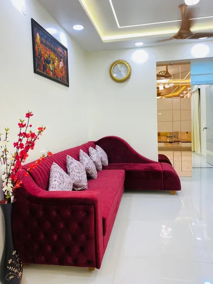 A finished living room featuring a luxurious tufted red velvet sofa. The space is designed for comfort and elegance, with a large art piece and a classic wall clock adding personal touches.