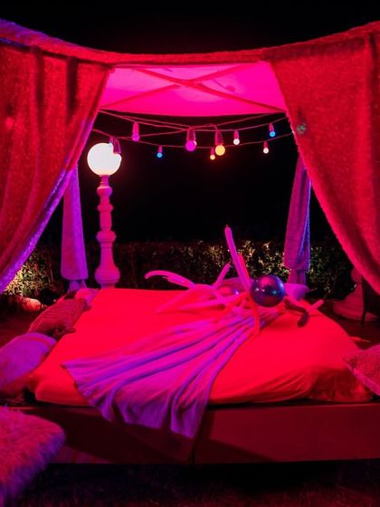 A glimpse of the after-party setup with a bed-like lounge under a canopy, lit with dramatic red lighting.