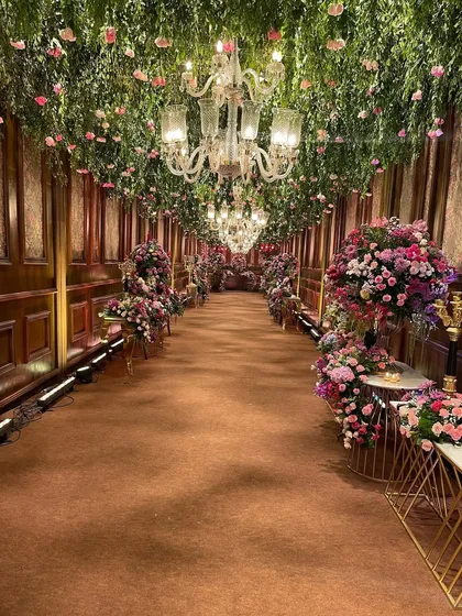 Imagine walking through a celestial garden. For this regal indoor wedding, I designed a breathtaking floral passage with a ceiling of cascading greenery and fresh pink blooms, lit by elegant crystal chandeliers to create a truly romantic and immersive entrance.