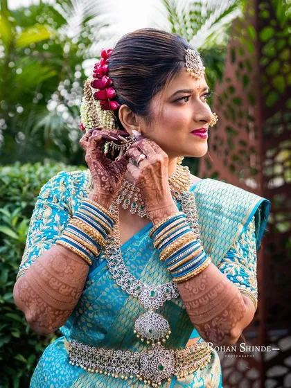 Amileen adjusting her earring, a candid moment that captures the beauty of her traditional attire and detailed henna.