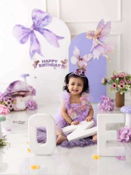 A happy birthday girl in her purple fairy-themed set, complete with a "Happy Birthday" sign and the number "ONE".