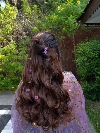 A back view of the Mehendi hairstyle, featuring a rose-shaped bun and small flowers scattered through the soft waves.