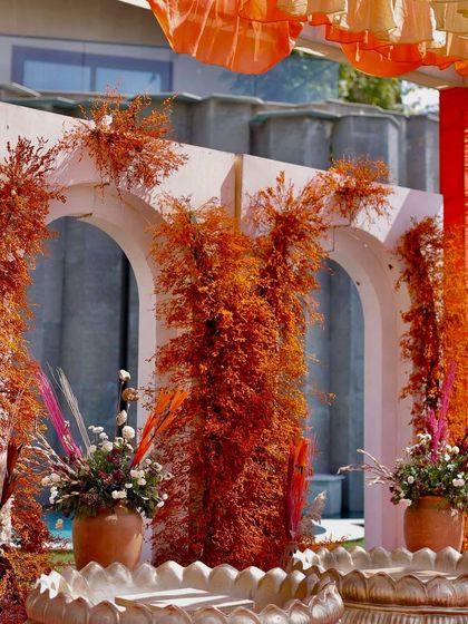 A close-up of the rust-orange Haldi decor, showing how the dried foliage is used to adorn modern white arches for a striking contrast.