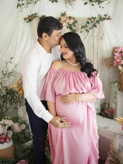 A tender kiss on the forehead speaks volumes. This intimate couple's portrait, set against a soft floral and macrame backdrop, is all about quiet love and anticipation.