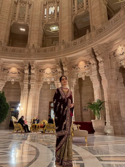 A full-length shot that captures the grandeur of both the palace and the royal velvet saree.