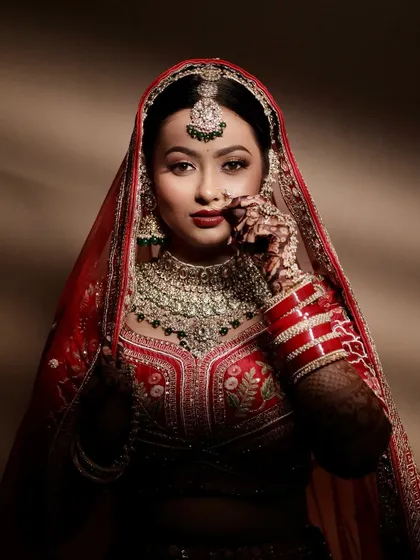 A powerful portrait of Krupa. The dramatic lighting highlights the flawless finish of her makeup and the regal elegance of her red bridal attire.
